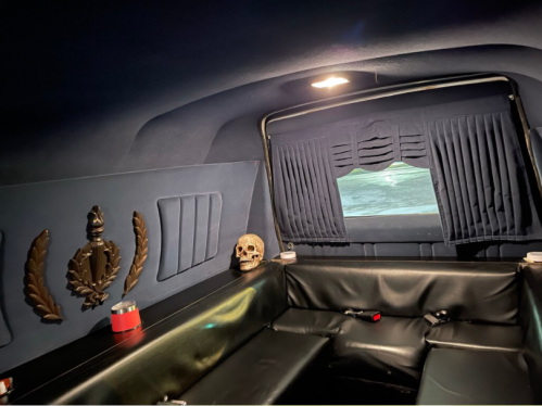 Interior of a dark, plush vehicle featuring black leather seating, curtains, and a decorative skull on the side.