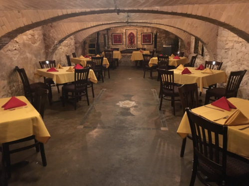 Cozy restaurant interior with yellow tablecloths and red napkins, featuring arched brick ceilings and stone walls.