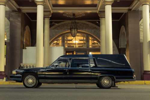 A black hearse parked in front of a grand building with tall columns and warm lighting.