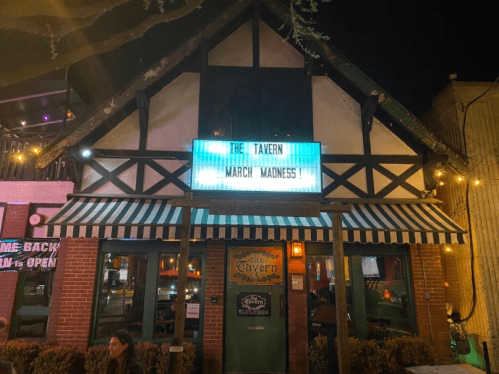 A lively tavern at night with a marquee sign advertising "March Madness" and festive outdoor lighting.