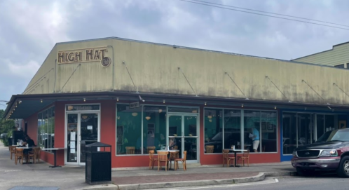 Exterior of High Hat restaurant with a green and red facade, outdoor seating, and a cloudy sky above.