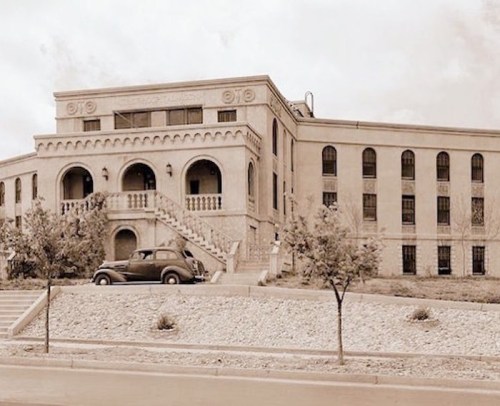 Historic building with ornate architecture, featuring a staircase and vintage car parked in front, set in a sepia tone.