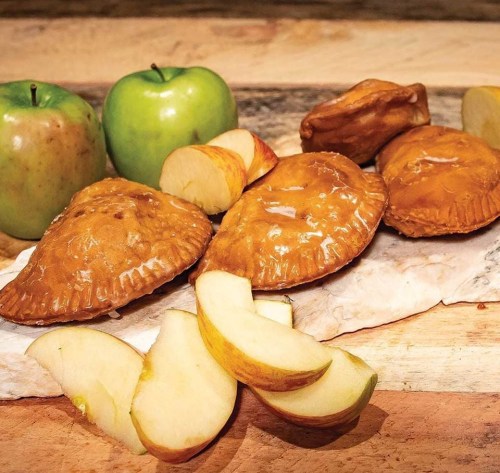 A wooden surface with green apples and sliced apples next to several golden-brown pastries.