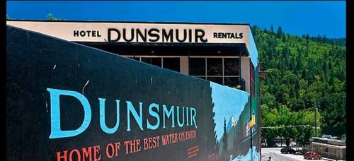 Sign for Hotel Dunsmuir with a colorful mural, surrounded by green hills and a clear blue sky.