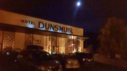 Nighttime view of Hotel Dunsmuir, illuminated sign, parked cars, and a bright moon in the sky.