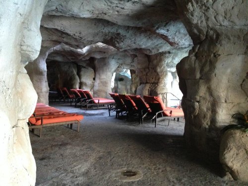 A cave-like interior with stone walls and orange lounge chairs arranged for relaxation. Natural light filters in.