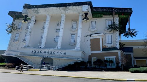 A large, upside-down building with columns and palm trees, labeled "WonderWorks," against a clear blue sky.
