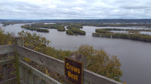 A scenic view of a river winding through lush greenery, with a sign reading "Crows Nest" in the foreground.