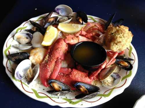 A seafood platter featuring lobster, clams, mussels, and a stuffed crab cake, garnished with lemon wedges.