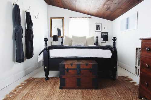 Cozy bedroom with a black bed, wooden chest, and warm decor, featuring a sloped ceiling and natural light.