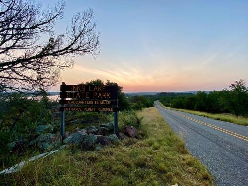 Sign for Inks Lake State Park at sunset, with a winding road and lush greenery in the foreground.