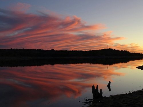 A serene sunset over a calm lake, with vibrant pink and orange clouds reflecting on the water's surface.