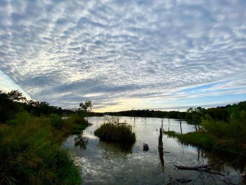 A serene landscape featuring a calm river, lush greenery, and a dramatic sky filled with clouds at sunset.