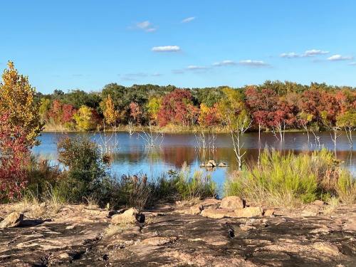 A serene lake surrounded by colorful autumn trees and rocky shoreline under a clear blue sky.