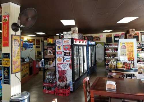 Interior of a vintage-style store with shelves of beverages, coolers, and retro advertisements on the walls.