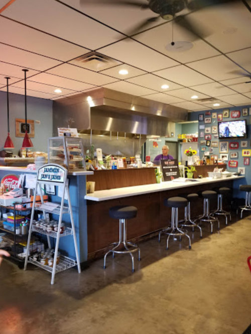 A cozy diner interior with a counter, stools, and colorful wall decor, featuring a chef and various food items.