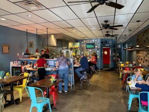 A cozy café interior with colorful chairs, patrons at the counter, and a child sitting at a table.