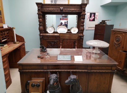 A vintage office setup featuring a large wooden desk, ornate mirror, and decorative items, including two dog figurines.