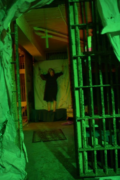 A dimly lit room with green lighting, featuring a figure on a backdrop, framed by prison bars.