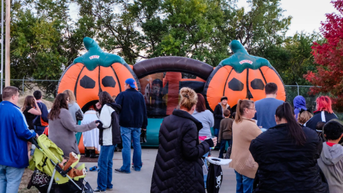 A crowd gathers around a large inflatable pumpkin-themed bounce house at an outdoor event.