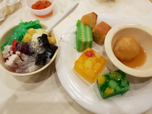 A bowl of colorful dessert with jelly, fruits, and a plate of assorted sweet treats, including cakes and a fruit ball.