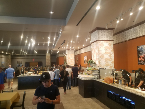 A busy restaurant interior with a buffet setup, patrons in line, and staff serving food in a warm, inviting atmosphere.