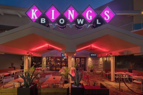 Exterior of Kings Bowl, featuring vibrant pink signage and modern seating under warm lighting.