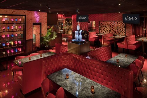 A stylish restaurant interior with red booths, marble tables, and colorful lighting, creating a vibrant atmosphere.
