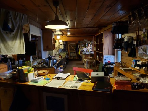 A cozy wooden interior of a shop with shelves, a counter, and various items for sale, illuminated by warm lighting.