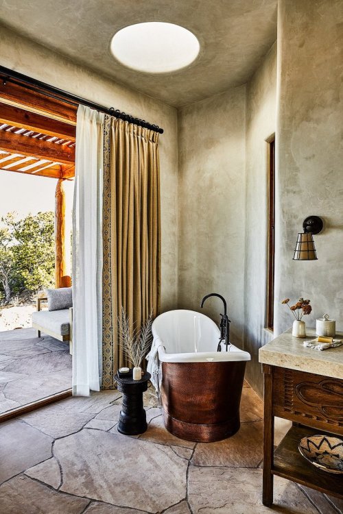 A modern bathroom featuring a freestanding tub, natural stone floor, and large window with a view.