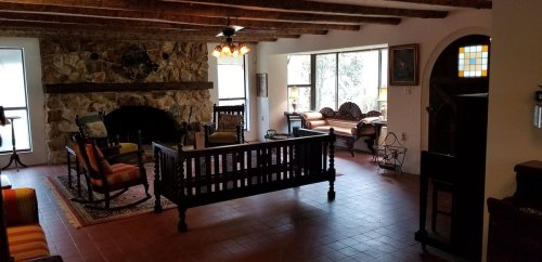 Cozy living room with stone fireplace, wooden beams, and large windows, featuring vintage furniture and warm lighting.