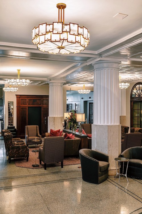 Elegant hotel lobby featuring plush seating, decorative chandeliers, and stylish columns. Warm and inviting atmosphere.