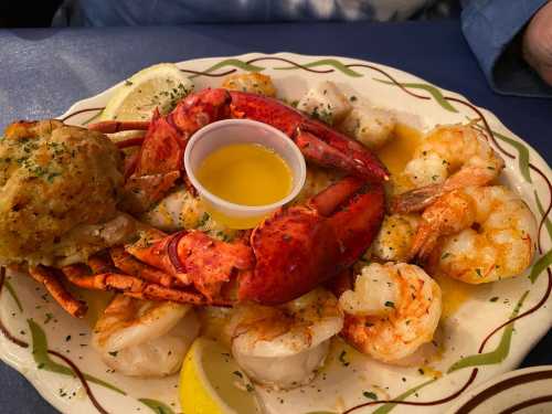 A seafood platter featuring a lobster, shrimp, scallops, and a side of stuffed crab, garnished with lemon and herbs.