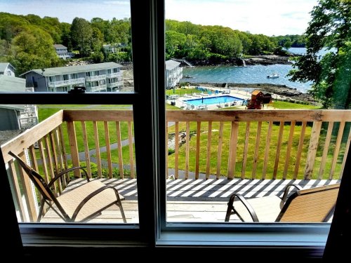 View from a balcony overlooking a pool, grassy area, and a scenic waterfront with trees in the background.