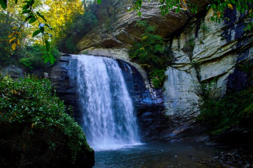A serene waterfall cascading over rocky cliffs, surrounded by lush greenery and trees in a tranquil natural setting.