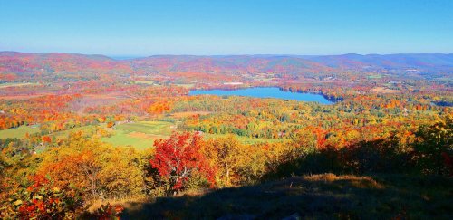 A vibrant autumn landscape featuring colorful trees, a serene lake, and rolling hills under a clear blue sky.