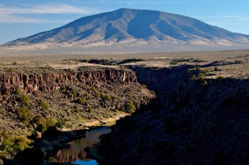 A vast landscape featuring a mountain in the background, with a river winding through rocky terrain in the foreground.
