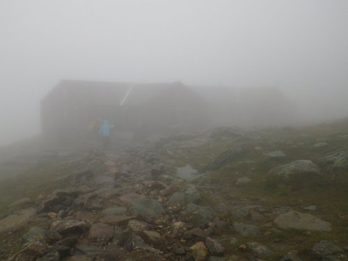 A foggy landscape with a rocky path leading to a distant building, partially obscured by mist.