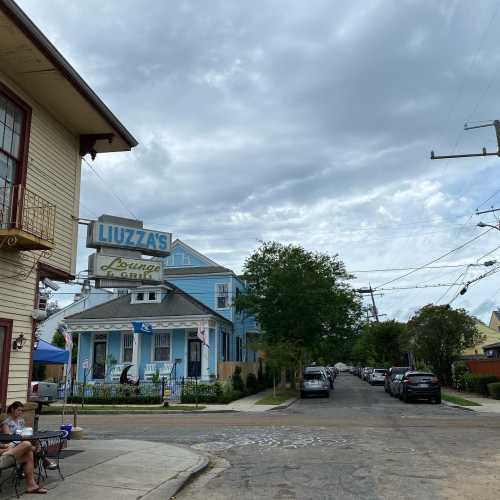 A street view featuring Liuzza's restaurant, with a blue building, trees, and parked cars under a cloudy sky.