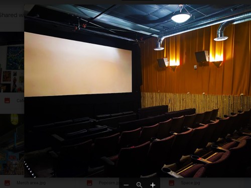 A dimly lit movie theater with empty seats facing a blank screen and warm-colored walls.