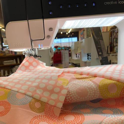 A sewing machine with a colorful polka dot fabric being stitched, set in a bright craft store.