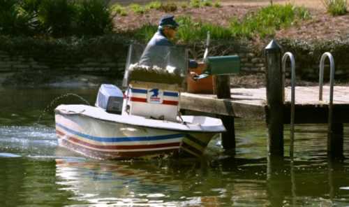 A person in a small boat approaches a wooden dock, holding a fishing rod and preparing to cast.