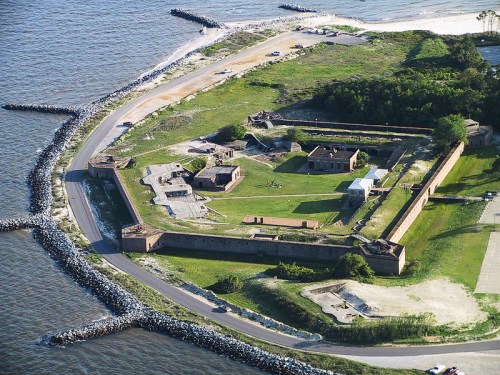 Aerial view of a historic fort surrounded by water, featuring grassy areas and remnants of old structures.