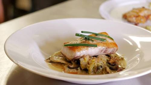 A plated dish featuring a seared fish fillet garnished with chives, served on a bed of sautéed vegetables.