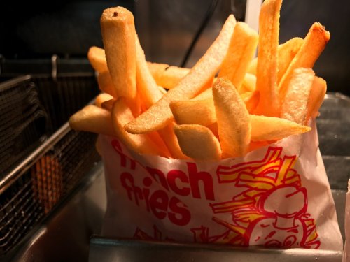 A serving of golden, crispy French fries in a paper bag with a colorful design.