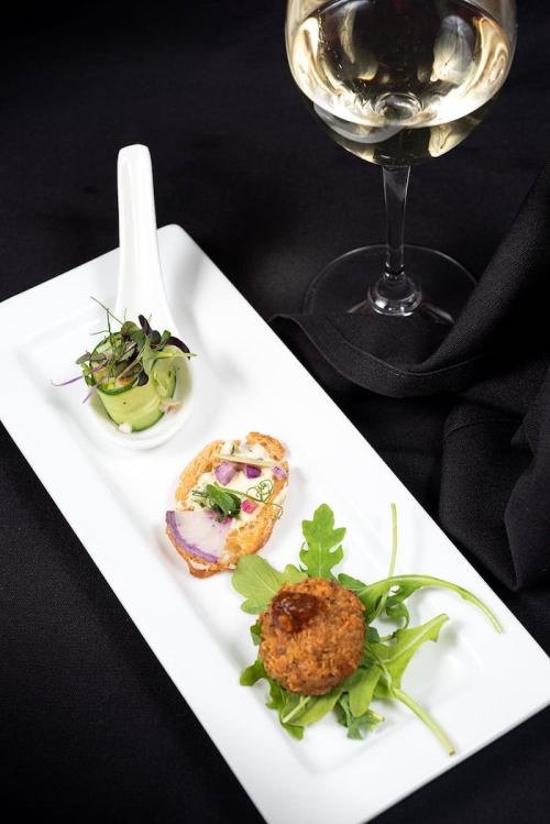 A gourmet plate featuring a small salad, a slice of bread with toppings, and a croquette, accompanied by a glass of white wine.