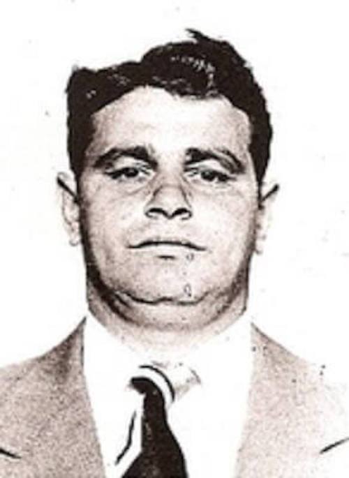 Black and white portrait of a man in a suit, looking directly at the camera with a neutral expression.