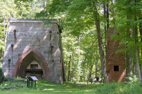Two historic structures in a lush green forest, one stone and one brick, surrounded by trees and walking paths.