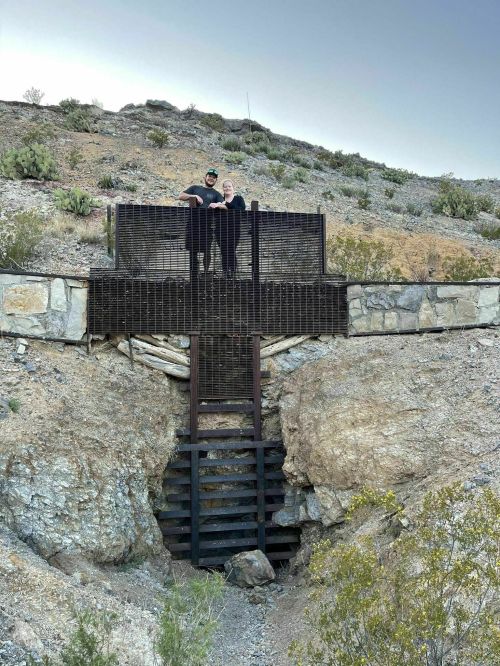 Two people stand on a metal platform overlooking a rocky hillside with stairs leading down into a ravine.