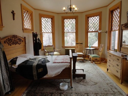 A cozy bedroom with a wooden bed, vintage furniture, and large windows, featuring a warm, inviting atmosphere.